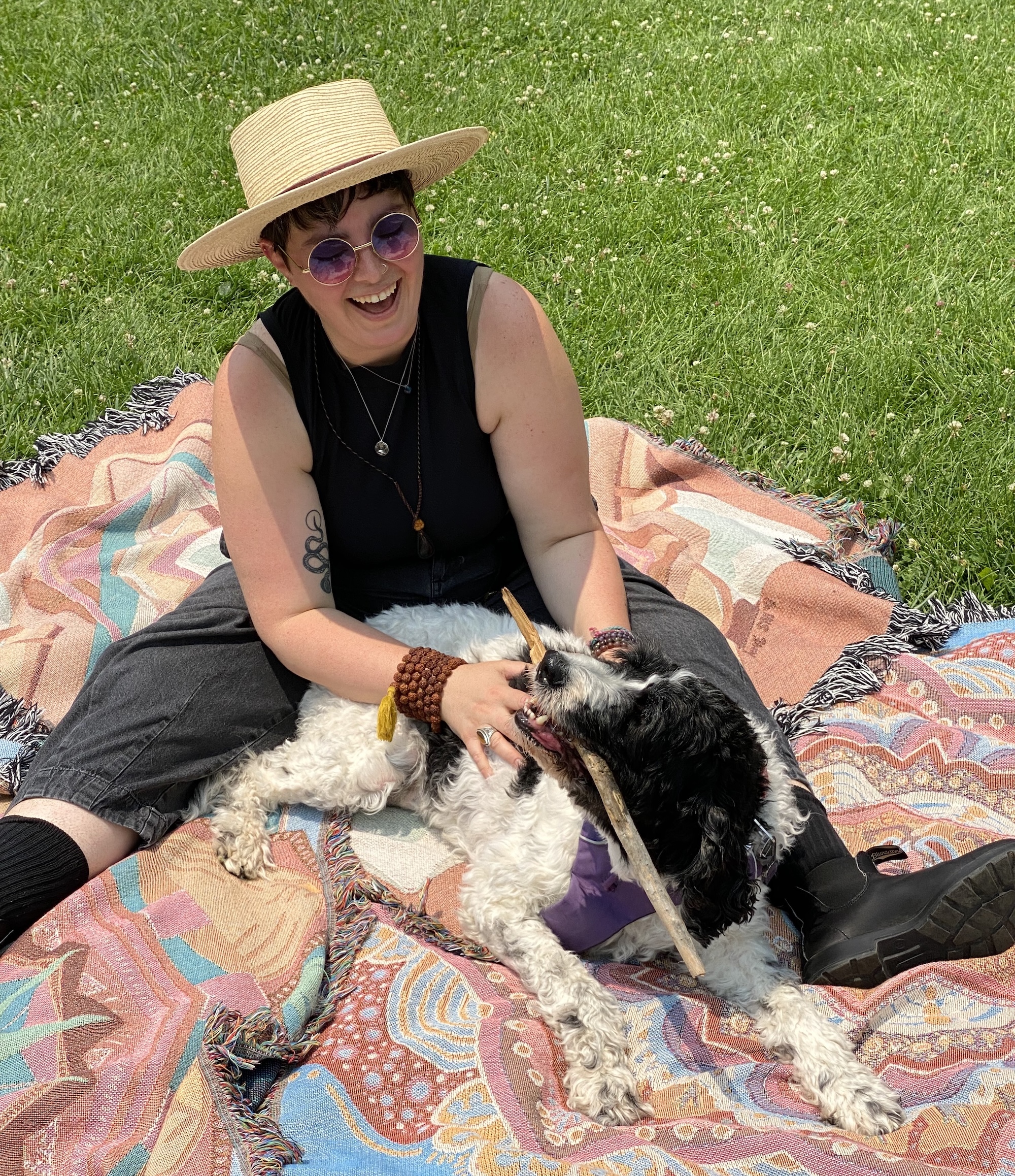 Mackenzie wears a sunhat, sitting on ritual blankets in a park with her dog, Peaches.