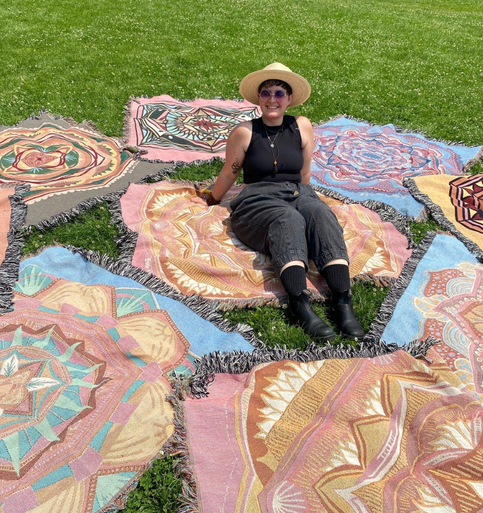 Mackenzie sits amongst colorful woven blankets on grass.